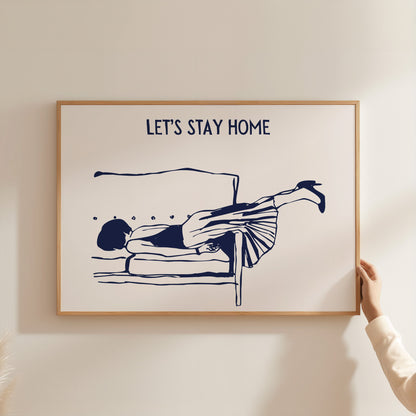 Framed artwork with a person lying on a bed and 'LET'S STAY HOME' text on a beige wall.