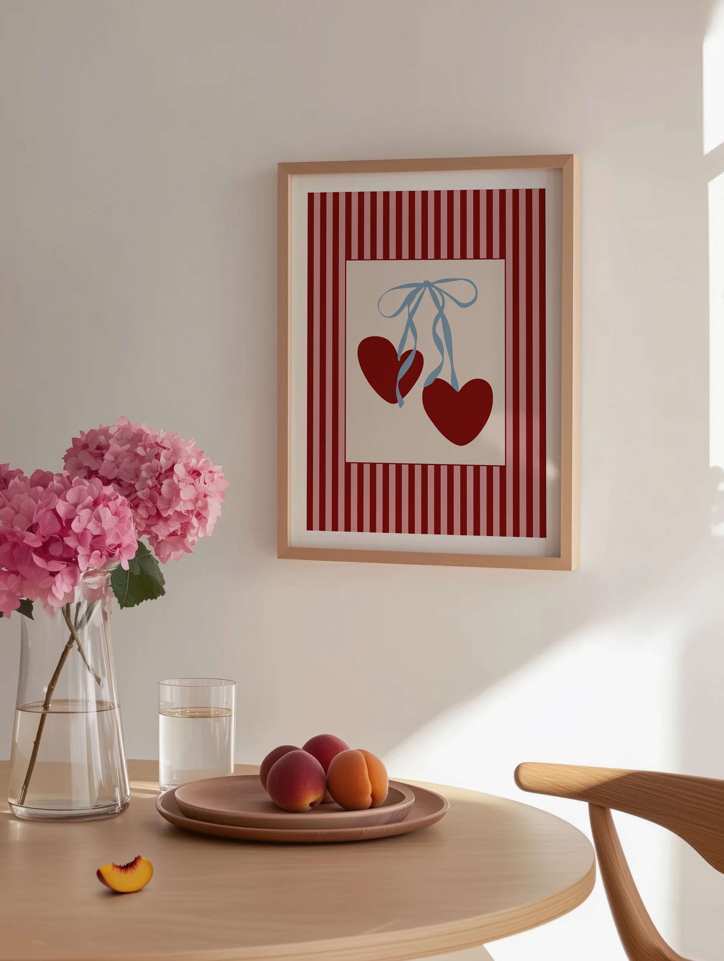 Framed artwork with red hearts on a wall above a table with flowers and fruit.